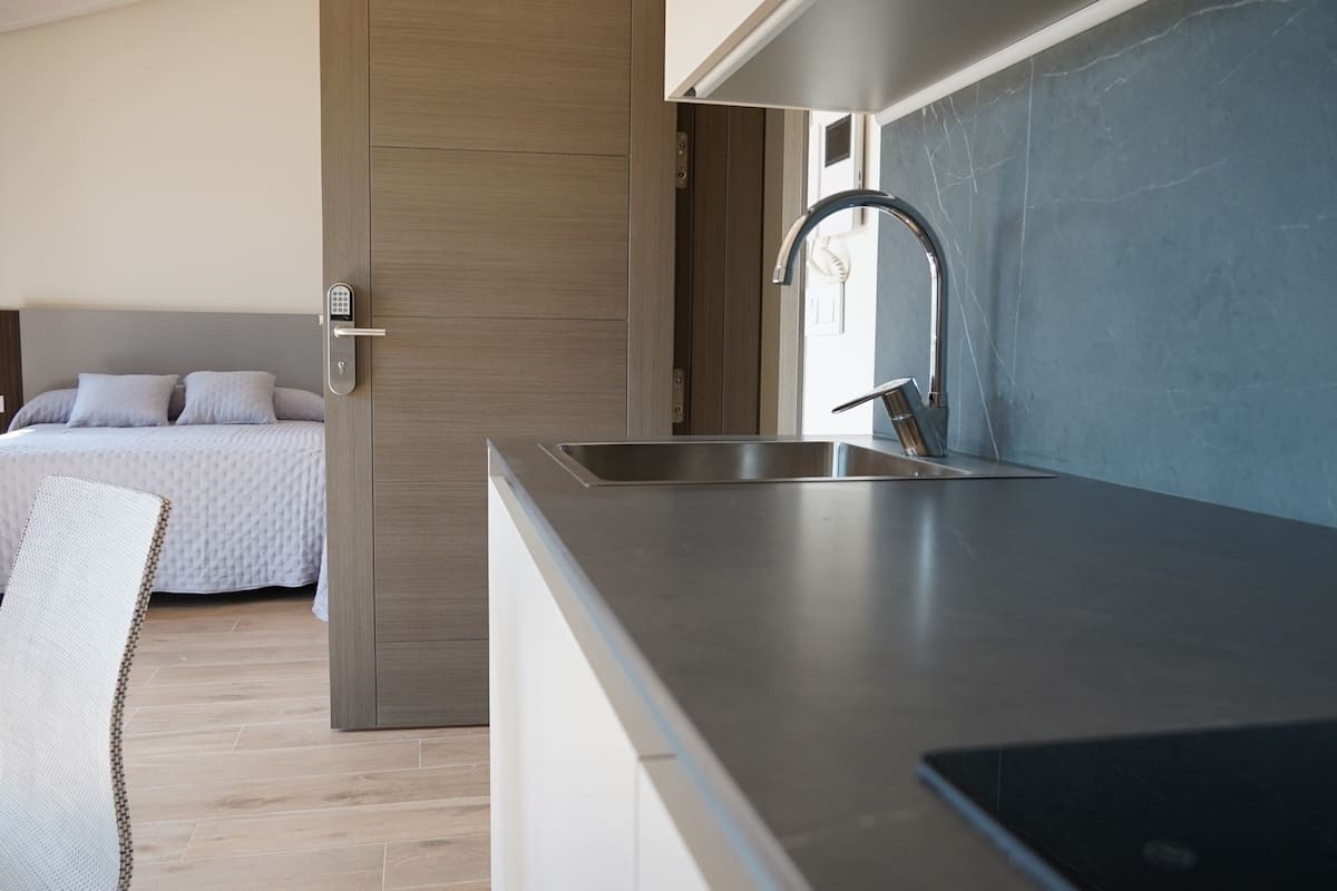 Una cocina moderna con pileta integrada y un dormitorio independiente con cama y mesita de noche.