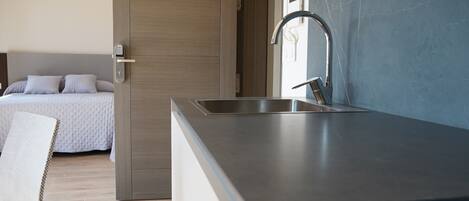 A modern kitchen with a built-in sink and a separate bedroom with a bed and a nightstand.