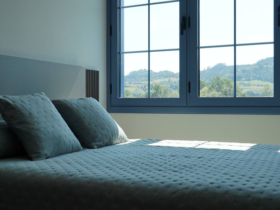 Un dormitorio con un ventanal grande, una cama con cubrecama acolchado y dos almohadas.