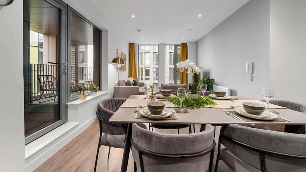 A modern dining area with a large table set for four, a sofa, and a view of the outside. - 3 Bed with Balcony | City Centre (Greater Manchester)
