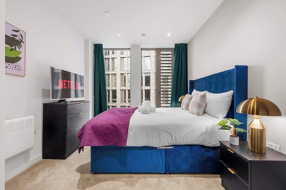 A modern bedroom with a bed, a TV, a dresser, and a nightstand with a lamp.