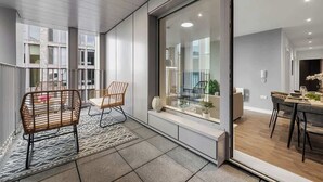 A modern interior with a dining area, a seating area with wicker chairs, and a view through a glass door. - 3 Bed with Balcony | City Centre (Greater Manchester)