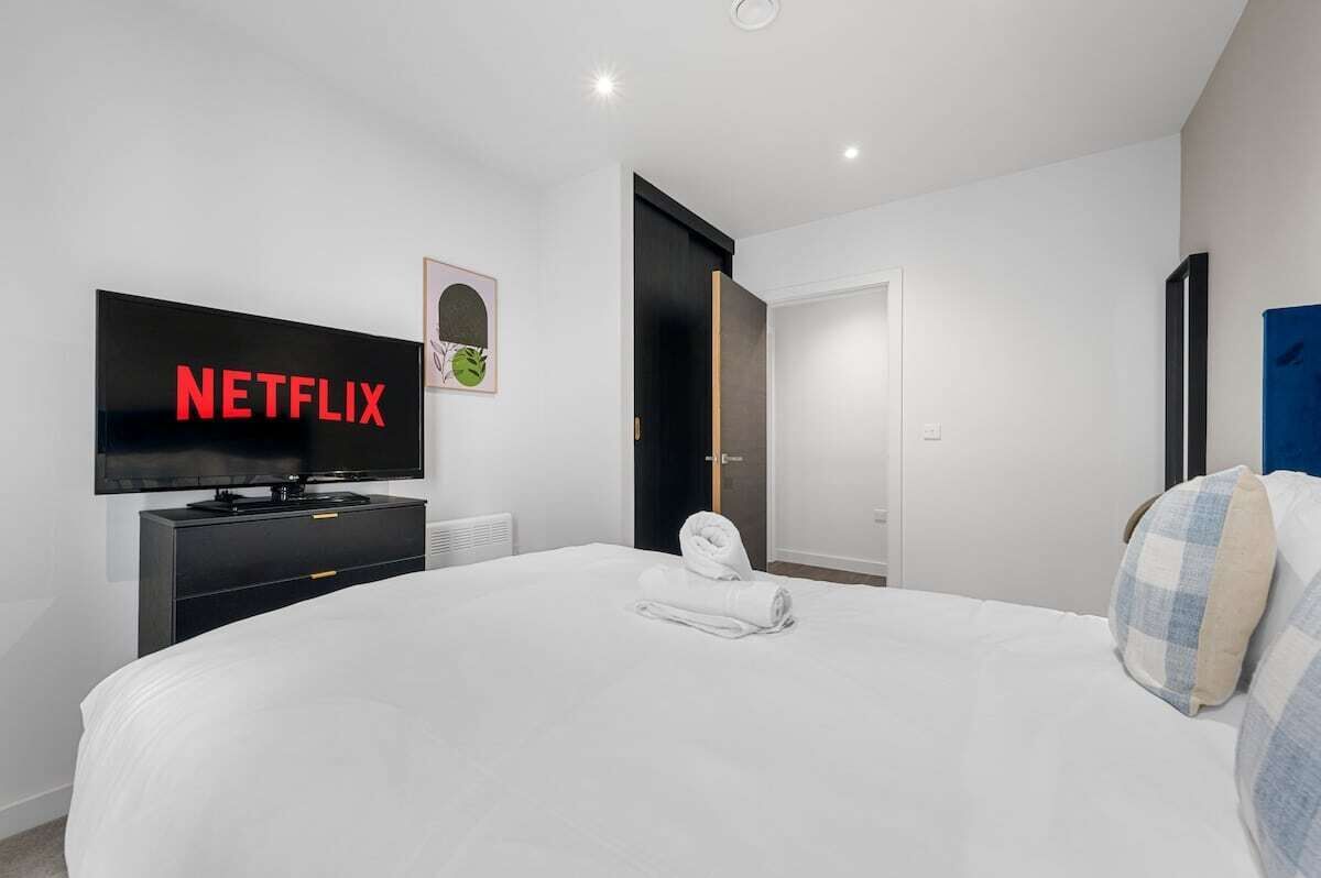 A hotel room with a bed, a TV displaying 'NETFLIX,' a door, and a wall-mounted artwork.