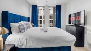 A hotel room with a large bed, a flat-screen TV, and a view of the city through the window. - 3 Bed with Balcony | City Centre (Greater Manchester)