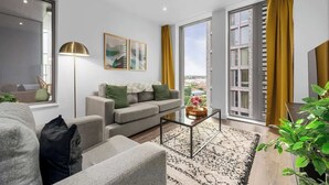 A modern living room with a sofa, coffee table, and large windows with curtains. - 3 Bed with Balcony | City Centre (Greater Manchester)