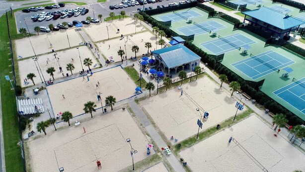Vista aérea de una zona de playa con varias canchas de tenis, un área de estar techada y un estacionamiento.