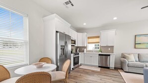Una cocina moderna con armarios blancos, electrodomésticos de acero inoxidable y un comedor con sillas de mimbre.