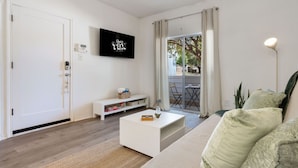 Un salon moderne doté d’un téléviseur à écran plat, d’un canapé blanc, d’une table basse et d’une porte-fenêtre coulissante donnant sur un espace extérieur.
