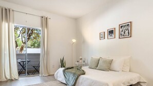 Une chambre à coucher comprenant un lit, une table de chevet, une lampe sur pied et donnant sur un balcon équipé d’une table et de chaises.