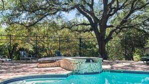 Une piscine avec un jacuzzi, entourée de chaises longues et d’un grand arbre.
