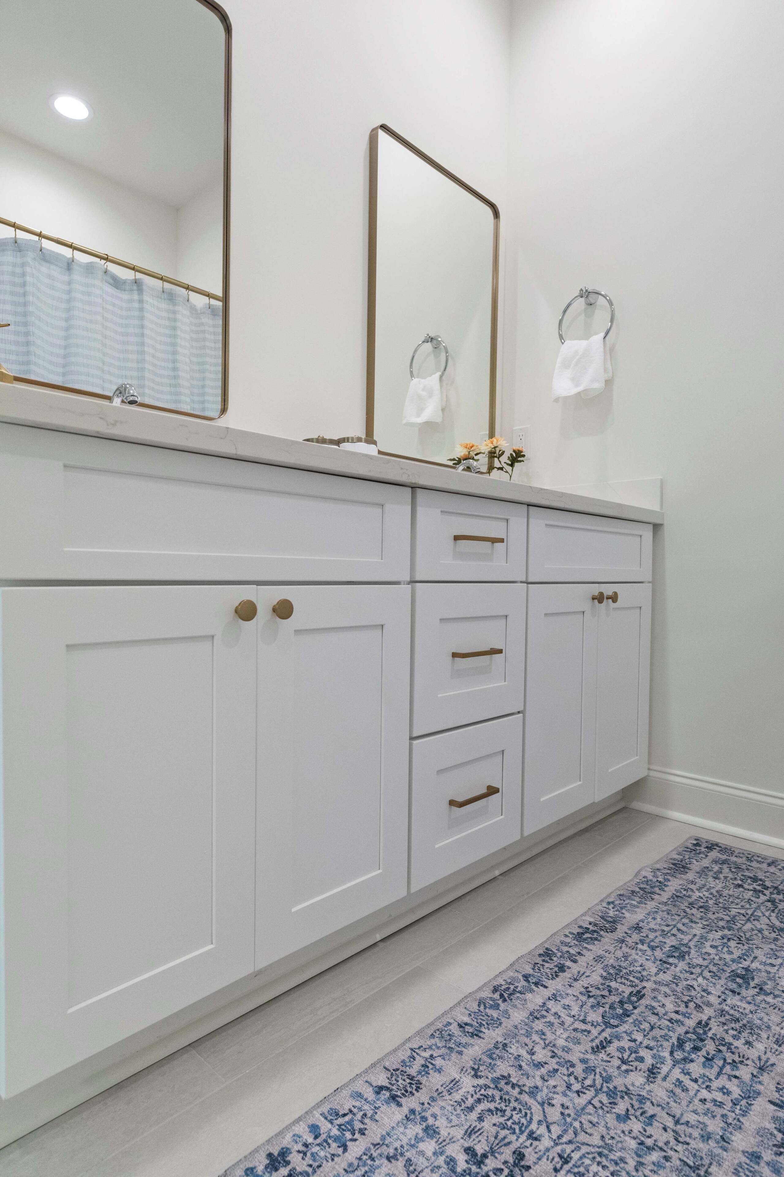 A bathroom with a white vanity, two mirrors, a shower curtain, and a blue patterned rug.