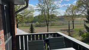 A patio with a table and chairs, a brick wall, and a view of trees and fields. - Hermine vacation apartment with far-reaching views of nature (Soltau)