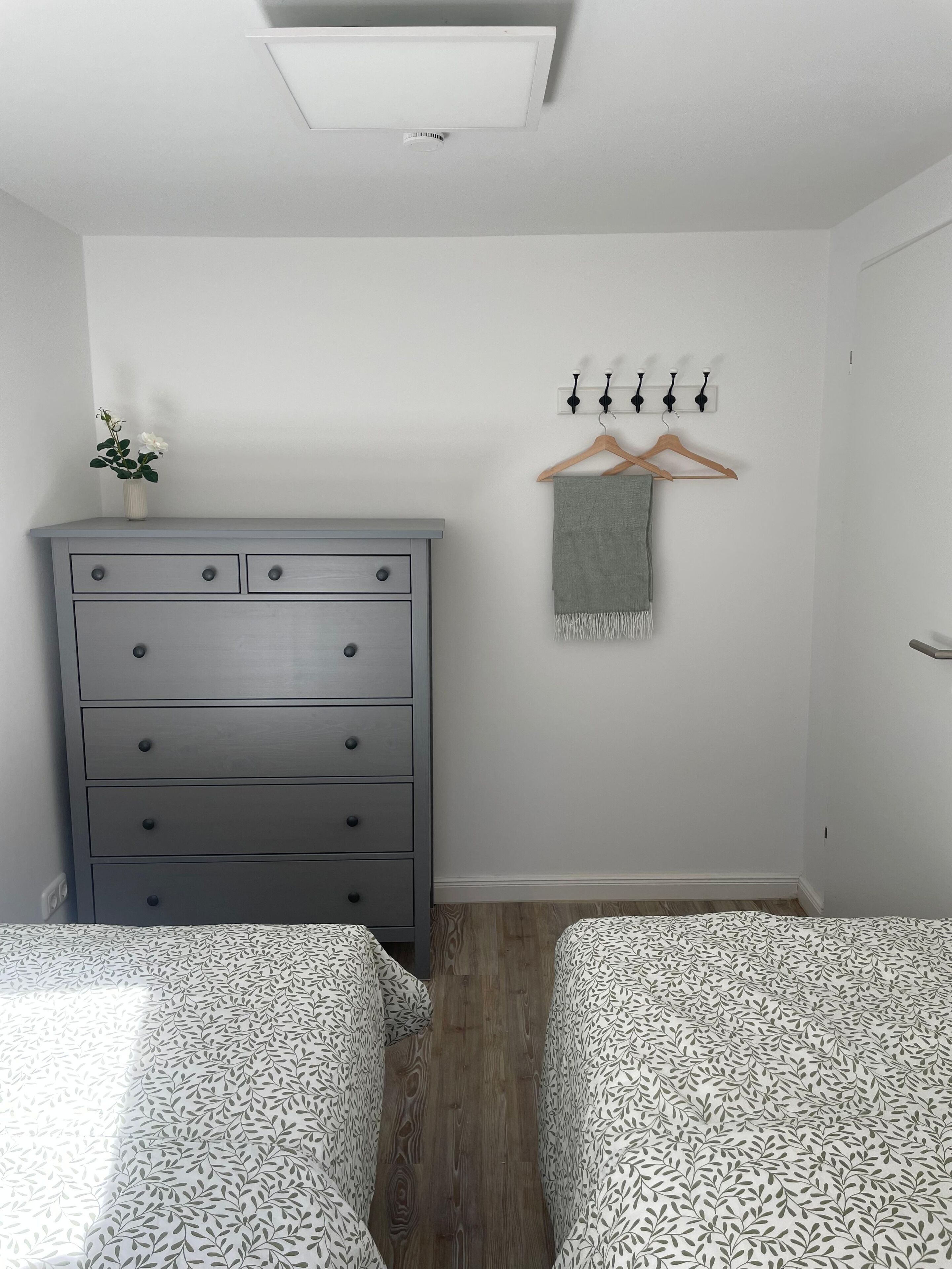 Un dormitorio con dos camas, un tocador, una planta y un perchero para toallas.
