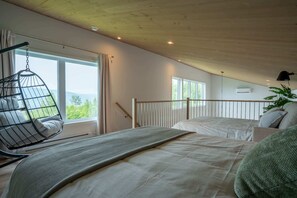 A bedroom with a bed, a hanging chair, and large windows.