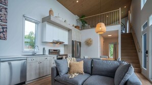A modern kitchen with white cabinets, a gray sofa, and a dining area with a wooden table. - Mountain View & Spa | Chalet Le Petit Leo (Saint-Côme)
