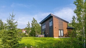 A modern two-story house with a sloped roof, surrounded by lush greenery and trees. - Mountain View & Spa | Chalet Le Petit Leo (Saint-Côme)