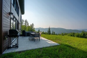 A patio with a grill and table, overlooking a grassy area and distant hills.
