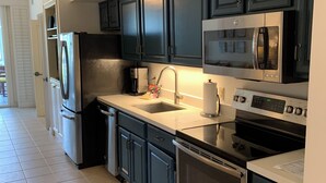 A modern kitchen with dark cabinets, stainless steel appliances, and a tiled floor. - Rare Beach Front Resort in Key West, Florida- 2 Bedroom/2 Bathroom! (Key West)