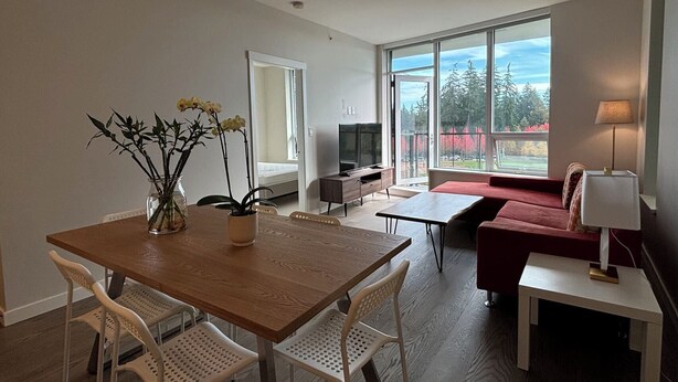 Una sala de estar moderna con una mesa de comedor de madera, sillas blancas, un sofá rojo y un televisor.