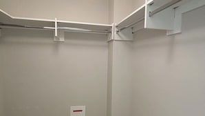 Un vestidor con paredes blancas, alfombra color beige y barras metálicas para colgar ropa.