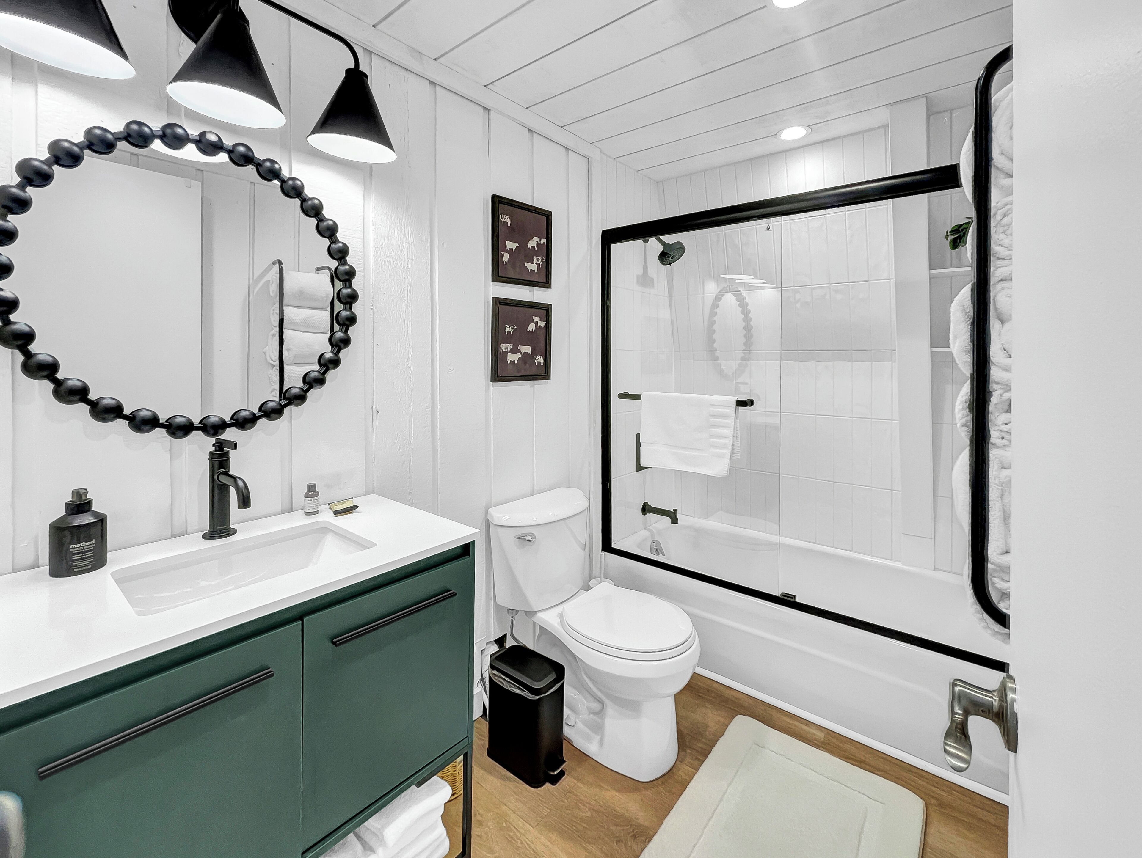 Un baño moderno con lavamanos blanco, gabinetes verdes, inodoro y zona de ducha con mampara de vidrio.