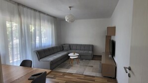 Una sala de estar moderna con un sofá seccional gris, una mesita redonda y un televisor sobre un mueble bajo.