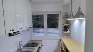 Una cocina compacta con armarios blancos, una encimera de madera y una ventana con persianas.