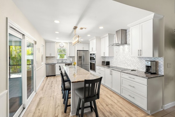 A modern kitchen with white cabinetry, a central island, and a view of greenery outside. - Sunset Beach Retreat w/Pool - 8 mins to Beach (Venice)