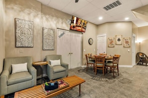 A living room with two armchairs, a coffee table, a dining table with chairs, a television mounted on the wall, and decorative wall art.