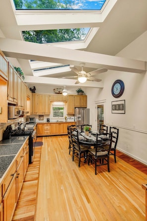 A modern kitchen with wooden cabinets, a dining area with a table and chairs, and a skylight above.