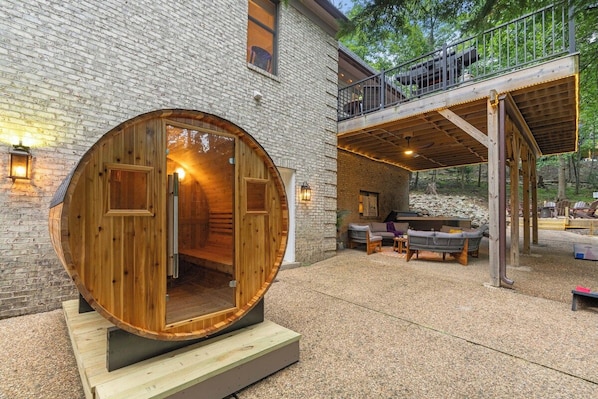 A wooden barrel-shaped structure with a door, a covered outdoor seating area, and a stone wall.