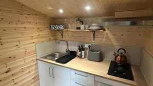 Une cuisine compacte aux murs en bois et dotée d’un plan de travail, comprenant un évier, une cuisinière et des placards de rangement.