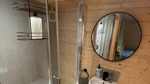 Une salle de bain avec une douche à parois de verre, un lavabo, des toilettes et un miroir rond accroché au mur.