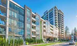 A modern multi-story building with large windows, a green lawn, and a clear sky. - UBC Ocean View Beautiful Unit (Vancouver)