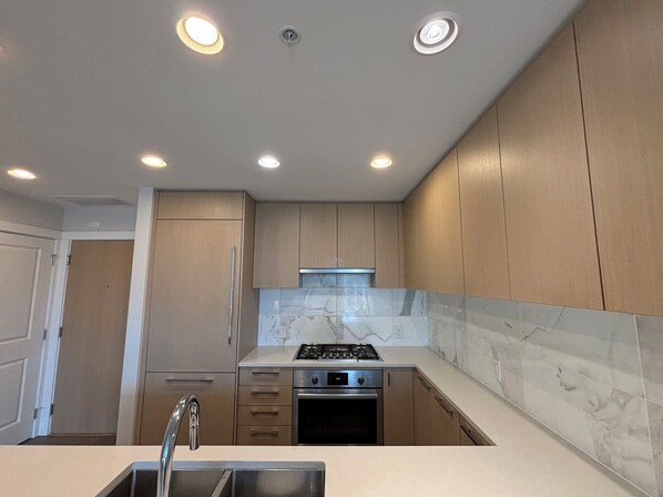 A modern kitchen with wooden cabinets, a stainless steel sink, a gas stove, and a built-in oven. - UBC Ocean View Beautiful Unit (Vancouver)