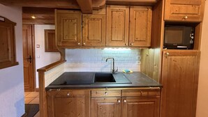 Een keuken met houten kastjes, een zwart aanrecht, een spoelbak en een magnetron.