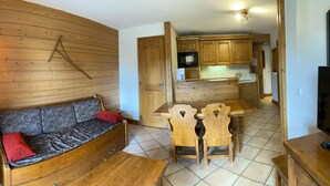 Ein gemütliches Wohnzimmer mit einer Couch, einem Esstisch mit Stühlen, Holzschränken und einer Küchenzeile.