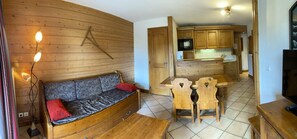 Ein gemütliches Wohnzimmer mit einer Couch, einem Esstisch mit Stühlen, Holzschränken und einer Küchenzeile.