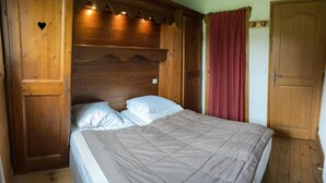 A bedroom with a wooden headboard, a bed with white bedding, and a red curtain. - 100m from ski slopes, Ground floor, view ski slopes, swimming pool, balcony, tv, ski locker, 42m² (Les Saisies)