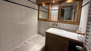 A bathroom with a white bathtub, wooden vanity, and a mirror above the sink. - 100m from ski slopes, Ground floor, view ski slopes, swimming pool, balcony, tv, ski locker, 42m² (Les Saisies)