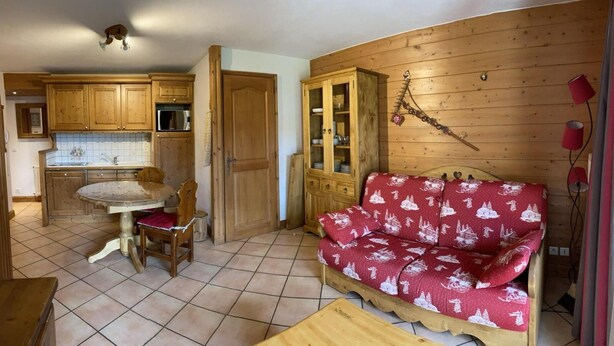 A cozy kitchen with wooden cabinets, a dining table with chairs, and a red sofa with a winter-themed cover. - 100m from ski slopes, Ground floor, view ski slopes, swimming pool, balcony, tv, ski locker, 42m² (Les Saisies)
