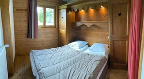 A wooden cabin bedroom with a bed, a window, and a door.