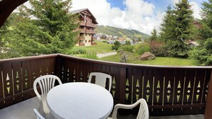 A balcony with a round table and four chairs, overlooking a mountainous landscape with a lodge in the background.