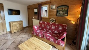 A cozy room with a wooden sofa, a small wooden table, a TV, and a framed picture on the wall.