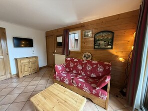 A cozy room with a wooden sofa, a small wooden table, a TV, and a framed picture on the wall.