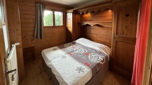 A wooden cabin bedroom with a bed, a window with curtains, and a door. - 100m from ski slopes, 2nd floor, swimming pool, balcony, tv, ski locker, 8m², Les Saisies (Les Saisies)