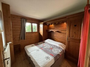 A wooden cabin bedroom with a bed, a window with curtains, and a door.