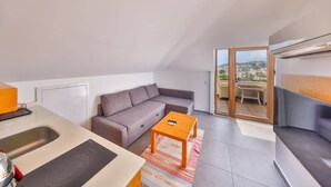 A modern apartment with a kitchenette, a gray sofa, a wooden coffee table, and a sliding glass door leading to a balcony with a city view. - THE PENTHOUSE WİTH TERRACE (Kas)