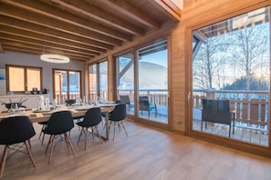 A dining area with a wooden table and chairs, large windows, and a view of a snowy landscape. - Elegant Alpine Retreat in Megeve Area (Praz-sur-Arly)