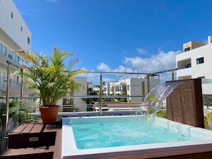 Piscina en la azotea con cascada, rodeada de plantas en macetas y edificios modernos.